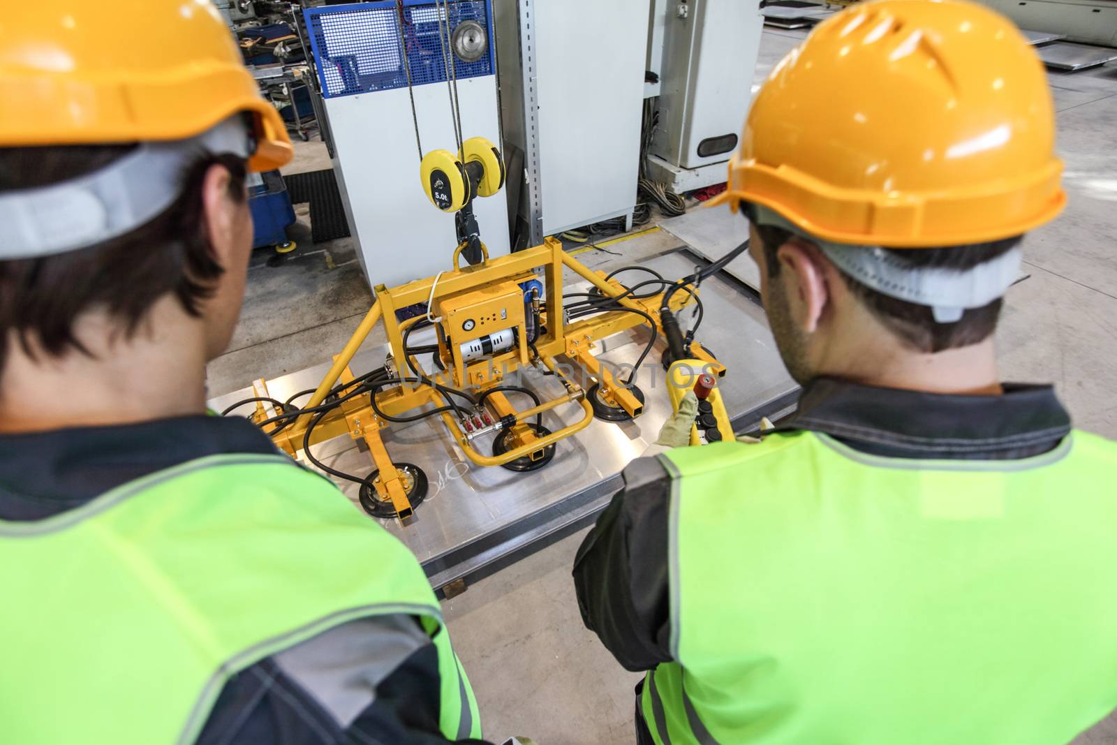 Workers near metal sheet lifting device at factory