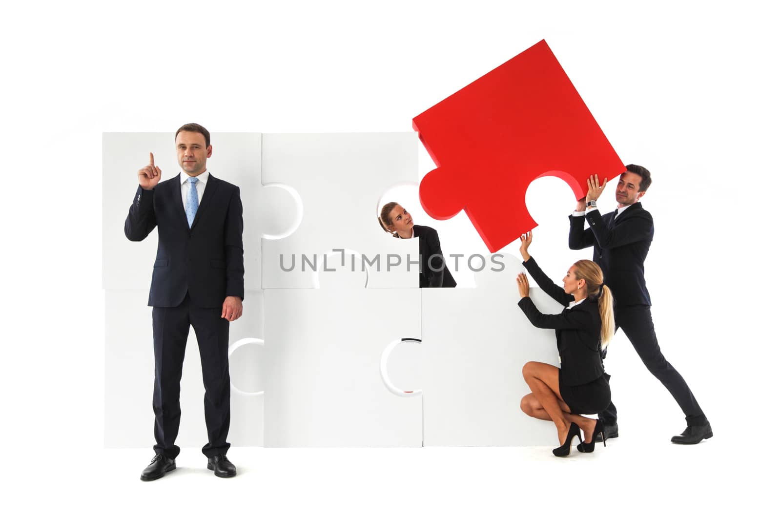 Business team assembling big puzzle and smart businessman standing aside pinting finger up isolated on white background