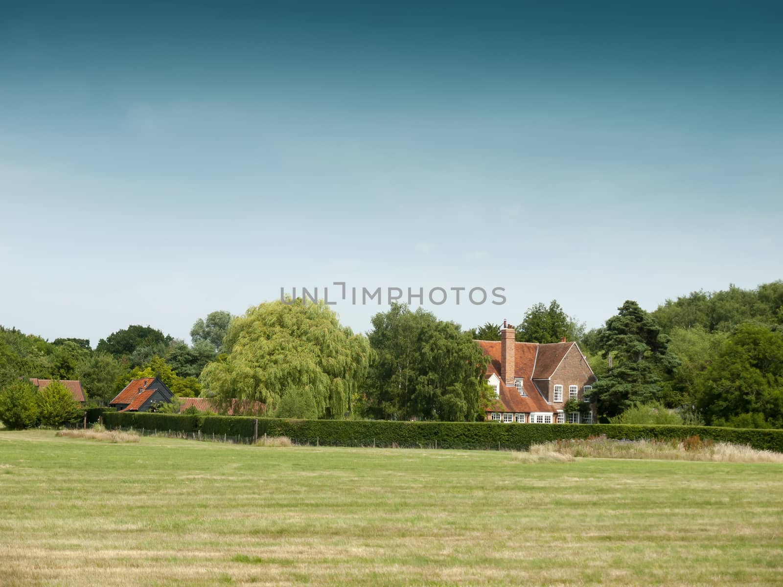 country farm house behind trees and field; Essex; UK