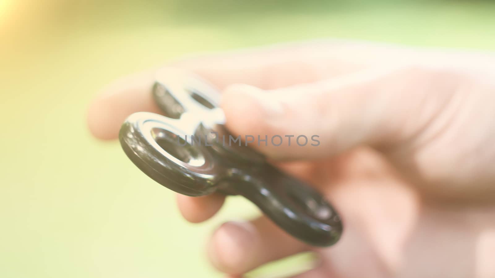 Playing with the black Fidget Spinner. Toy spinner in hand. Sun effect.