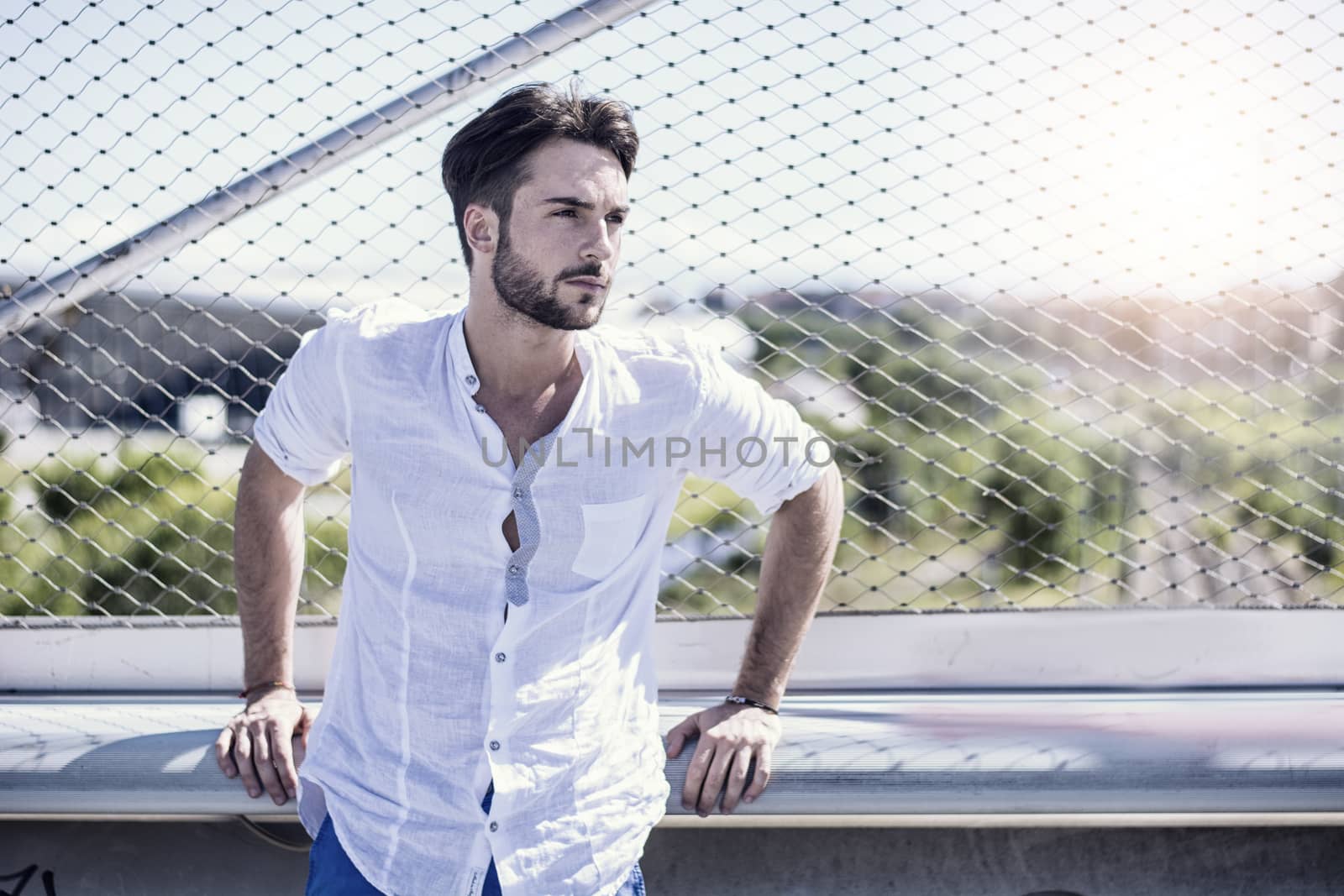 One handsome young man in urban setting in European city, standing against metal grid