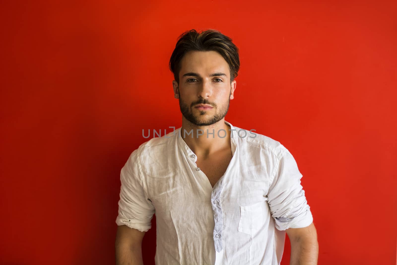 Stylish trendy young man standing outdoor against red wall, looking confindent at camera