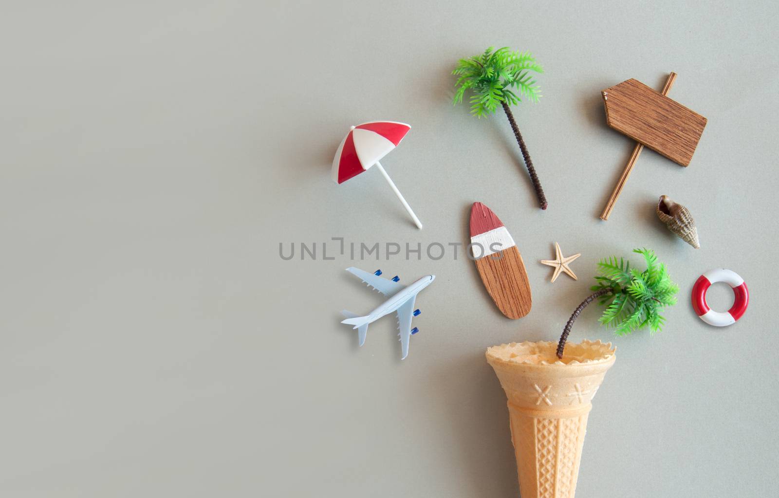 Icecream cone with various summer items including parasol, surfboard, miniature airplane and pine trees 