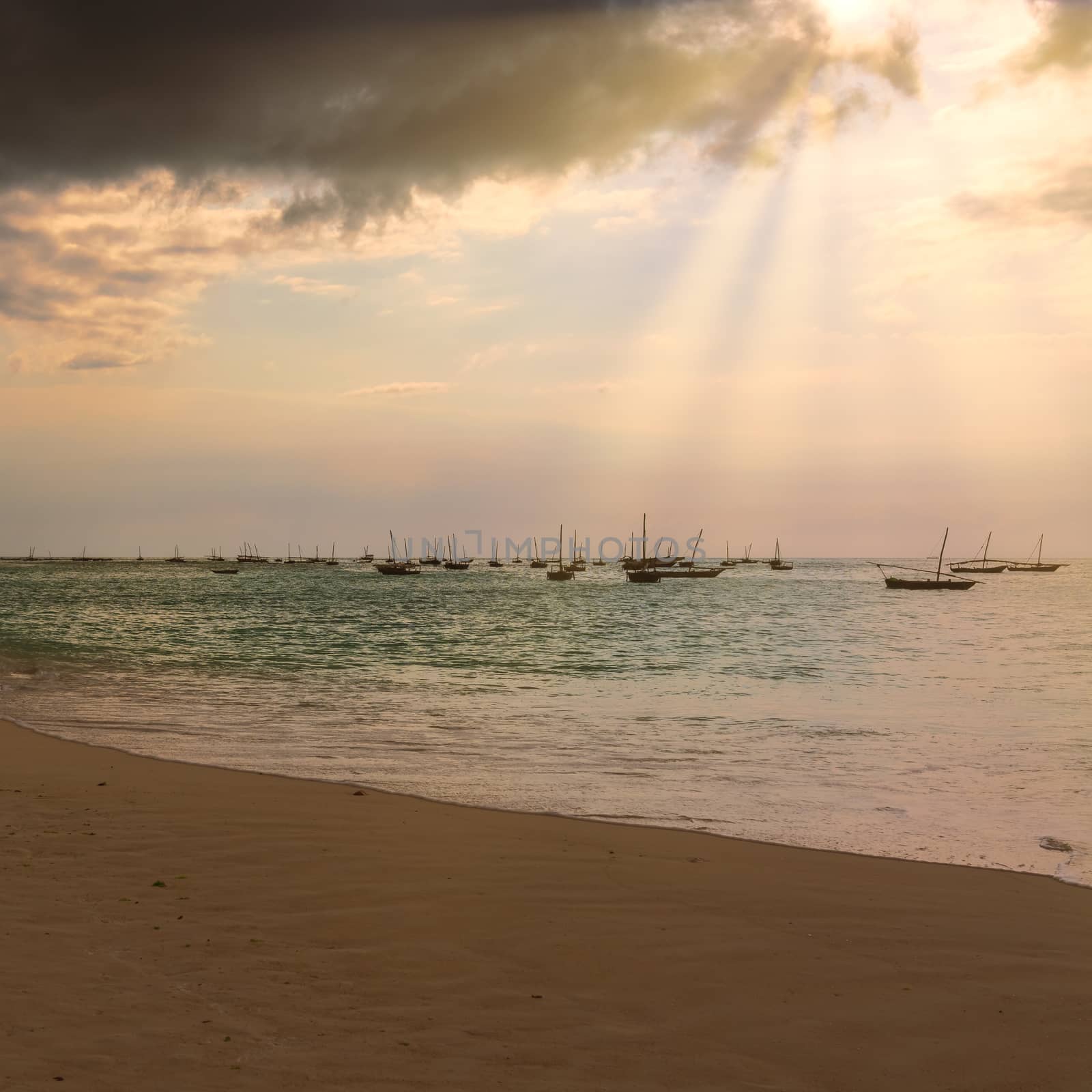 Several fishing boats silhouette anchored out in the ocean off the coast of Zanzibar, at sunset  with sunbeams.