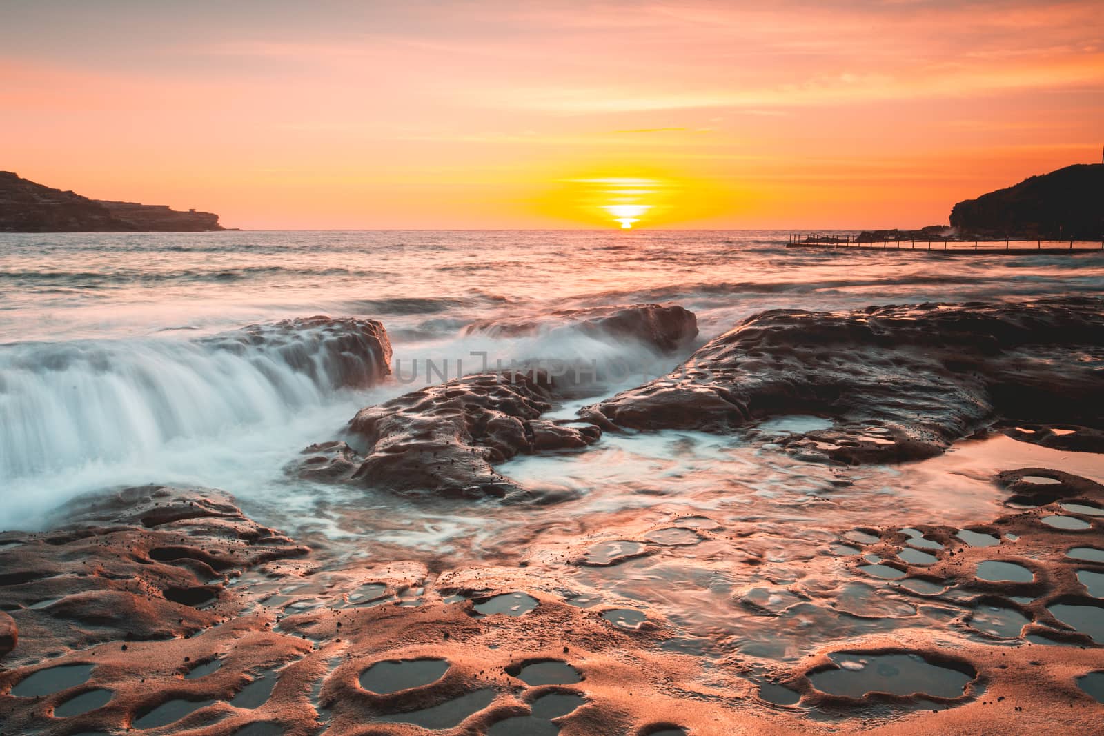 Summer sunrise light up the sky in warm tones and cast its beautiful light over the sea coast.  Australia