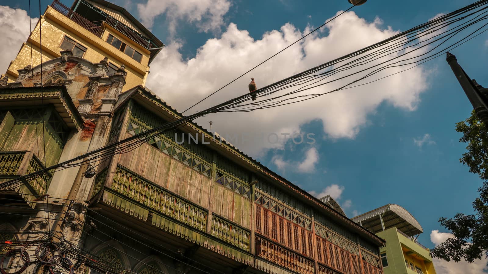 Ancient Wooden House with a Bird on Electric Wires. Low Angle View. Bright Sunny Sky with Clouds.