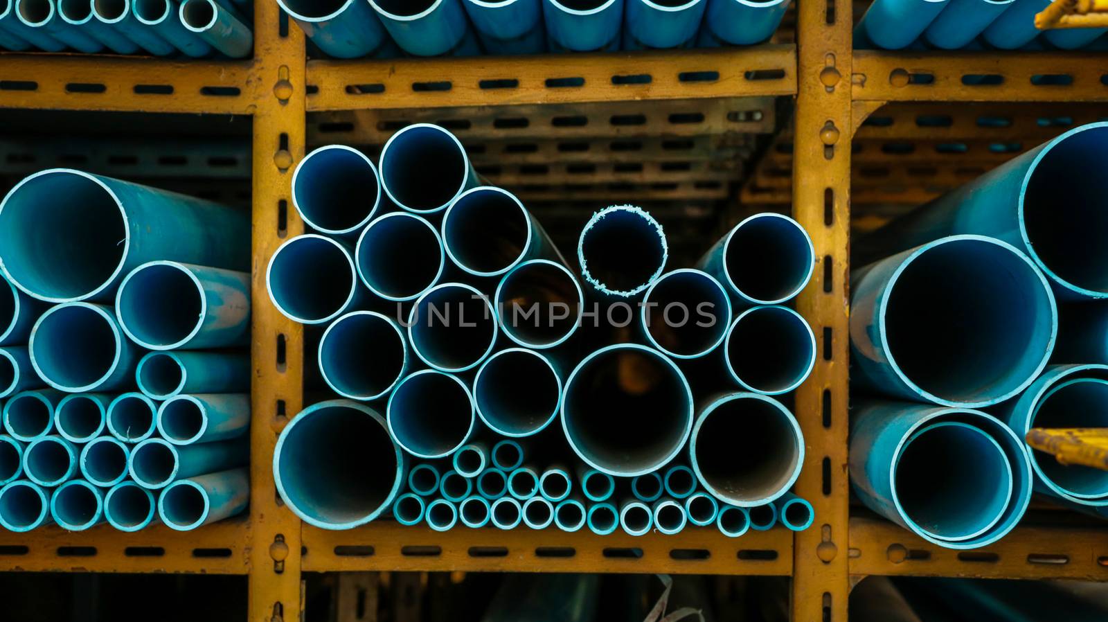 Different Sizes of Blue Water Pipes on Yellow Metal Rack. Eye Level View.
