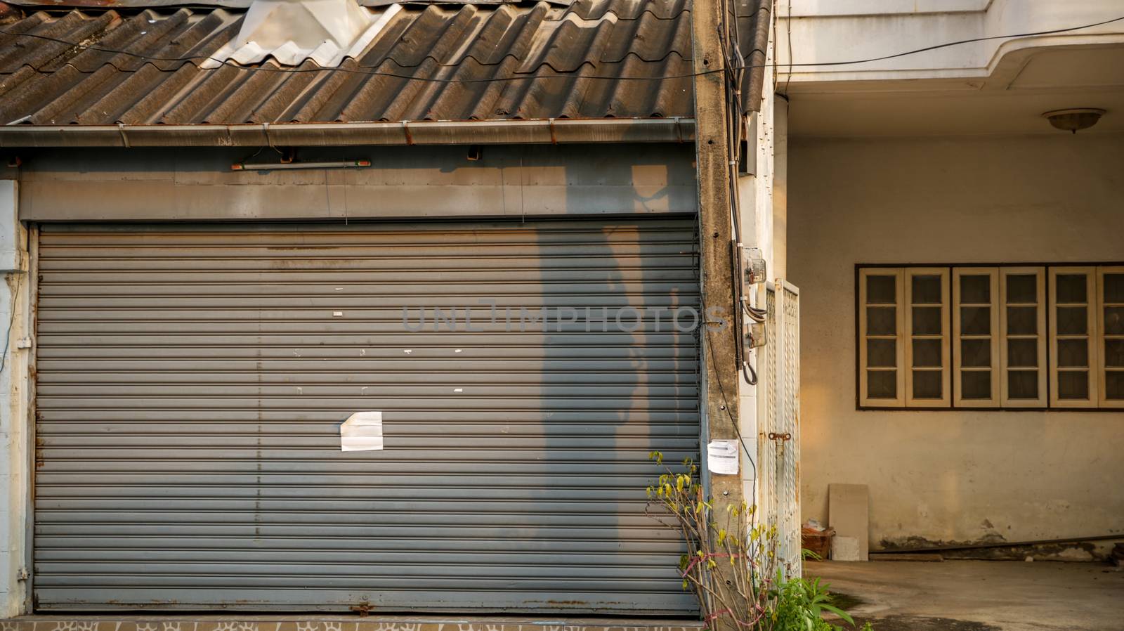 Dirty Vintage Roller Shutter Door with Blank Paper Note - Old Abandoned House for Sale  in Bangkok Thailand. Sunny Warm Day