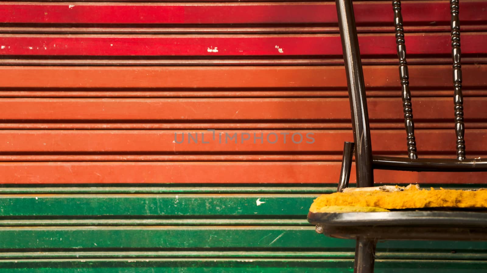 Abandoned Vintage Metal Chair with Colorful Roller Shutter Door/ Corrugated Iron Background. Outdoor Garage/ Junkyard. Street Photography. Bangkok, Thailand.