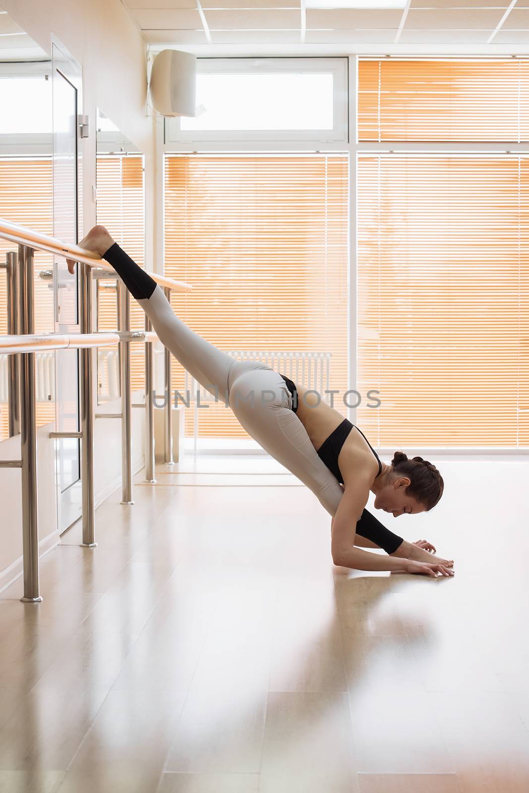 Young woman in sportswear performing stretching exercise near ballet barre while training in studio