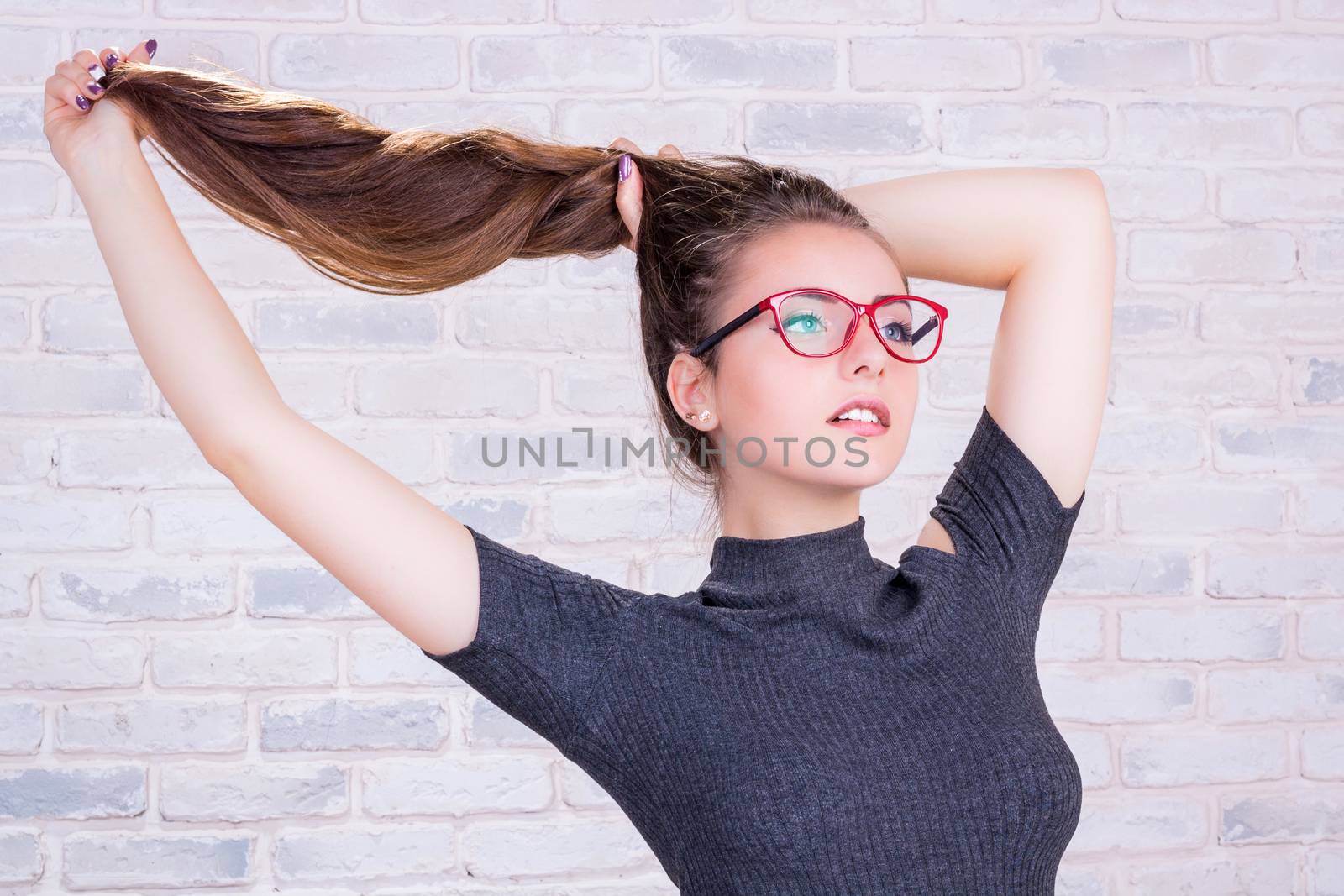 Young beautiful girl model with long hair in grey dress pulls her hair tail