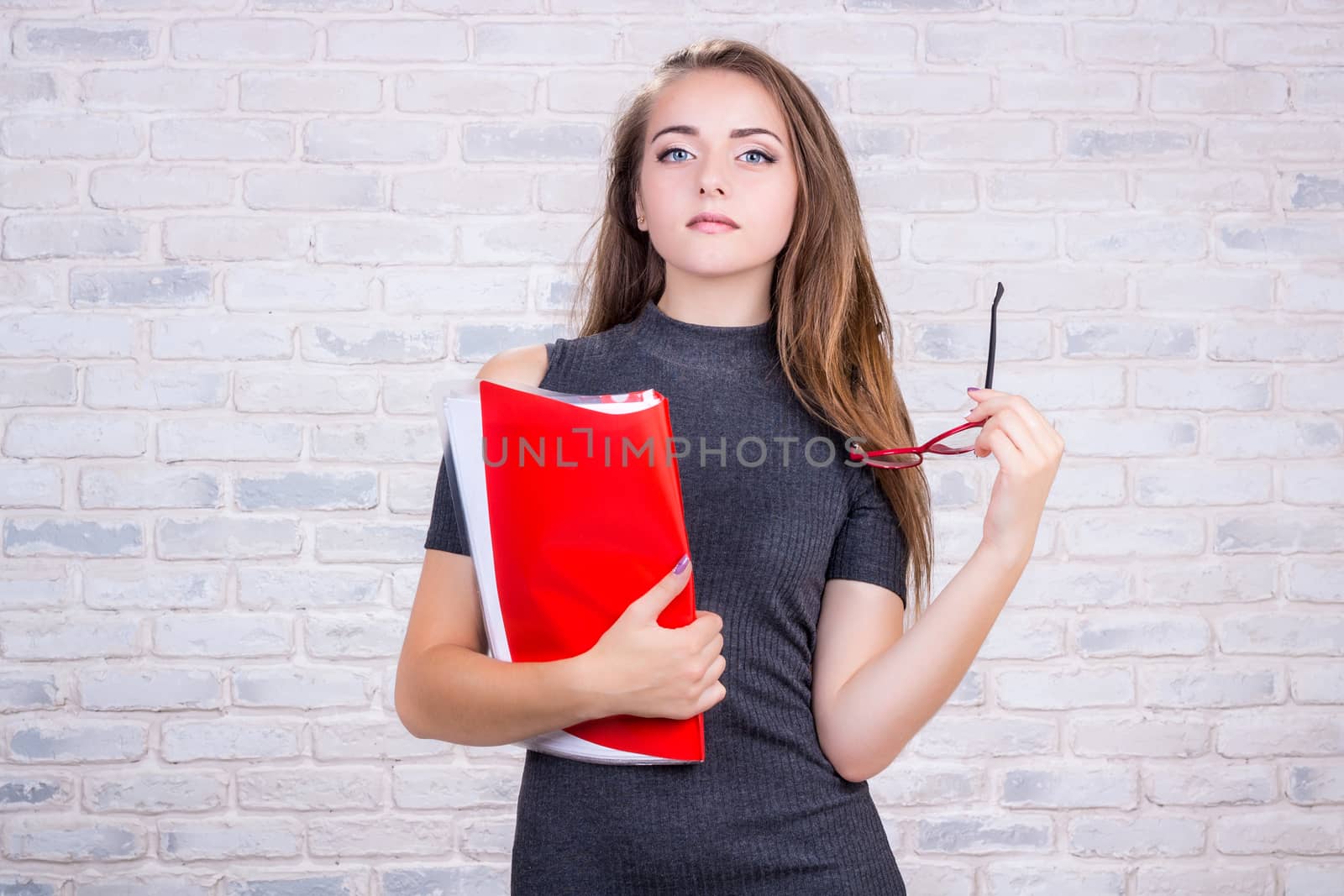 Young beautiful girl model with long hair imitates business lady, office manager or administrator with red folder of documents