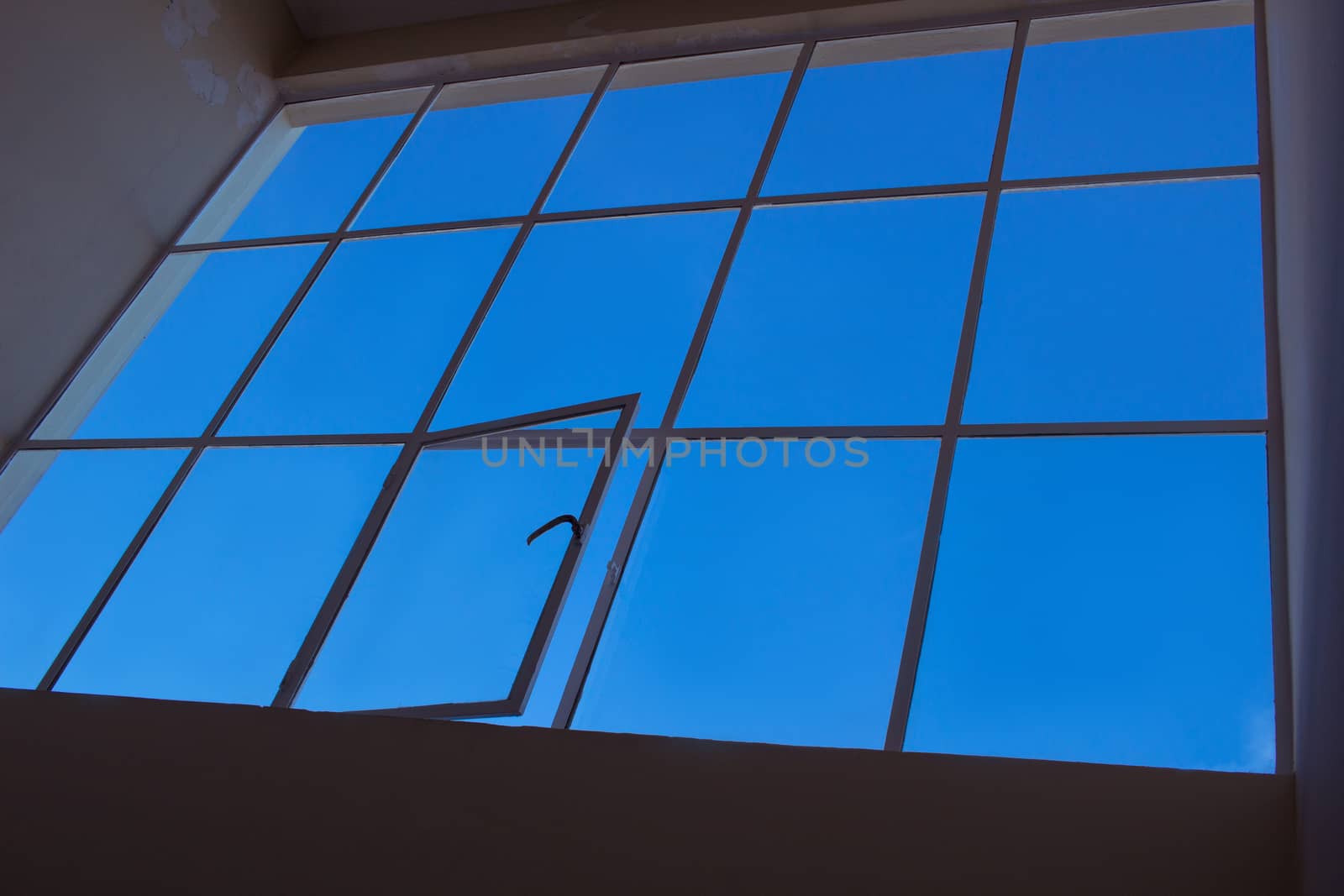 Blue sky view through big loft upper window with transparent glass cells and open leaf