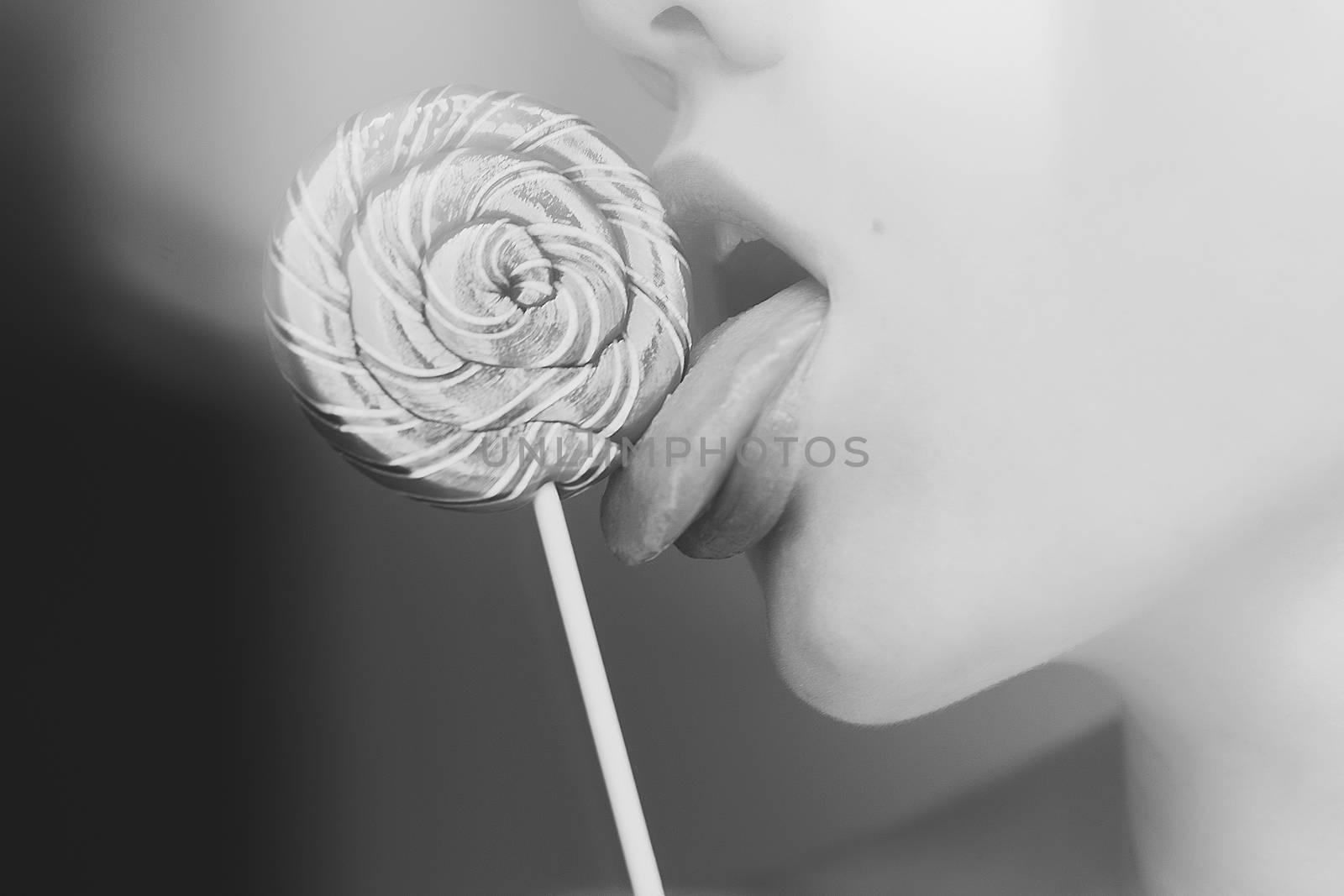 Crop side view of faceless slender woman licking twisted orange lollipop