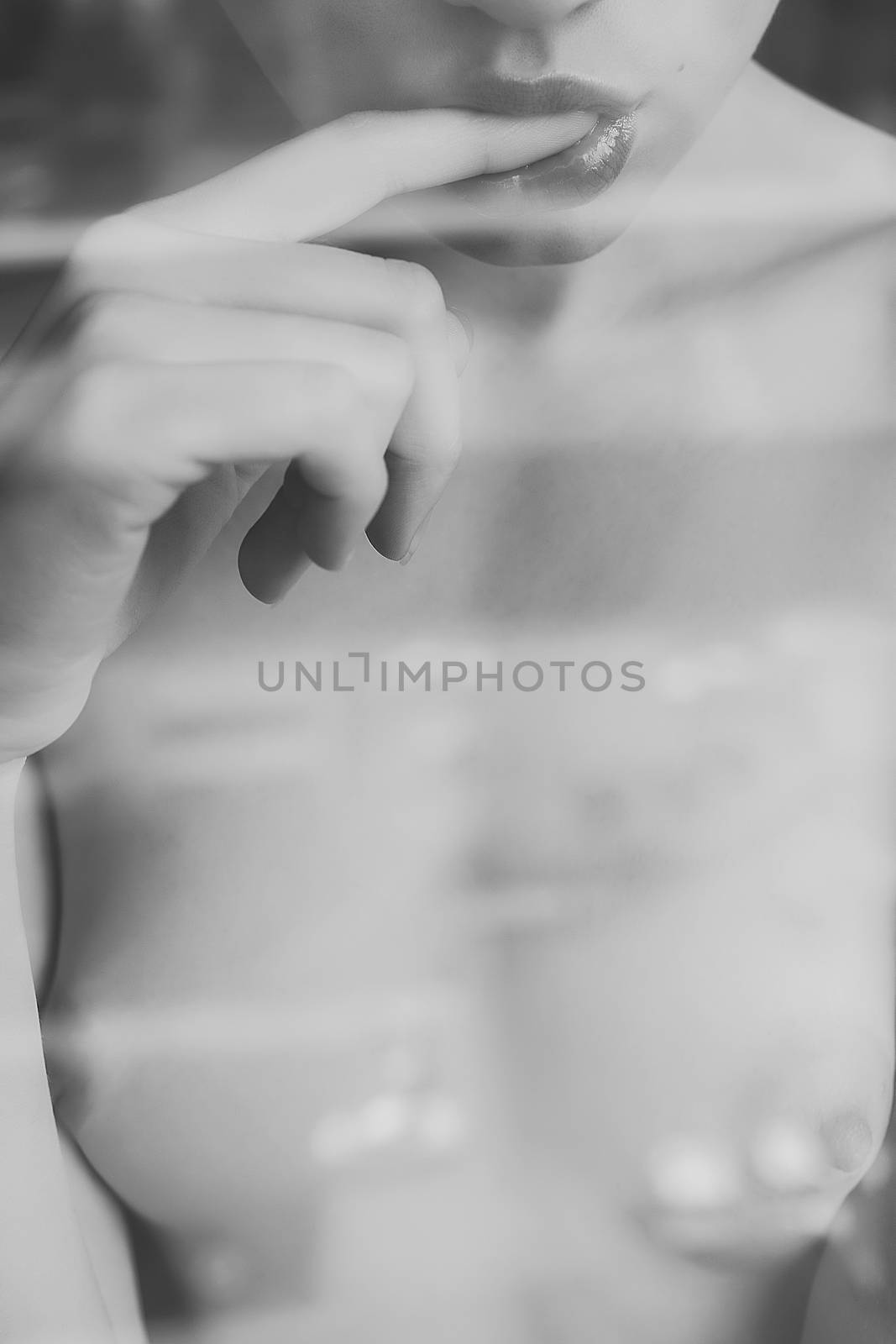 Crop view through glass of faceless naked young woman sexually putting finger in mouth