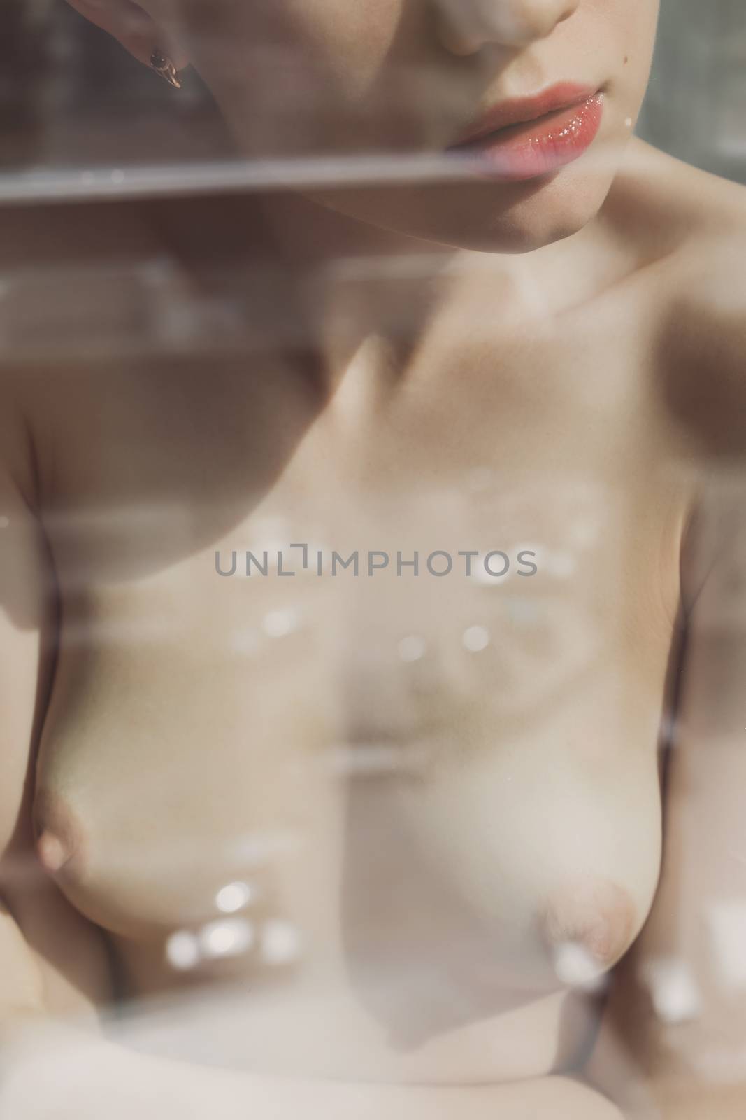 Crop view through glass of anonymous young woman with naked chest