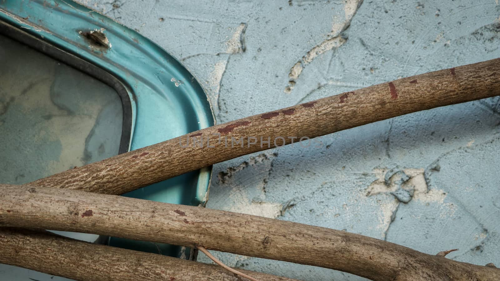 Abandoned Car Window Frame with Logs on Rough Painted Teal Wall - Garden/ Junkyard. Rural Thailand.