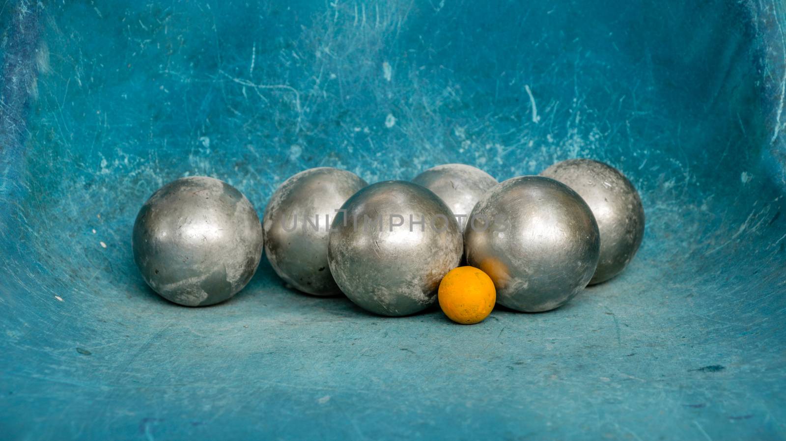 Shiny Metal Petanque Balls and Yellow Wooden Ball on Blue/ Teal Plastic Chair - Scratching Texture. Complementary color scheme