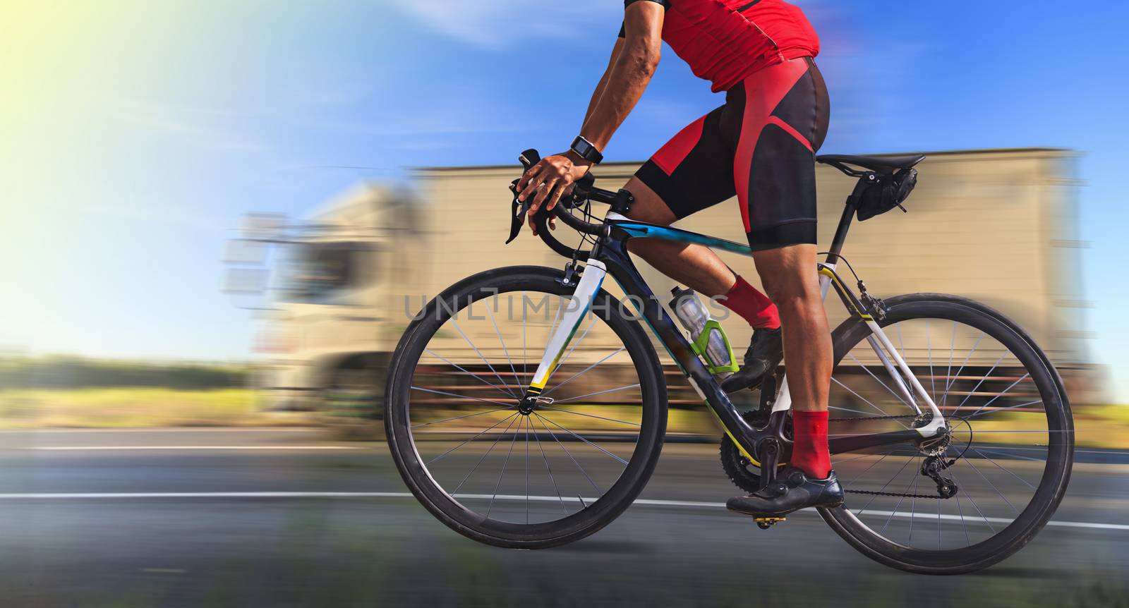 Man on a bicycle on a road with motion blur of truck on highway at morning light