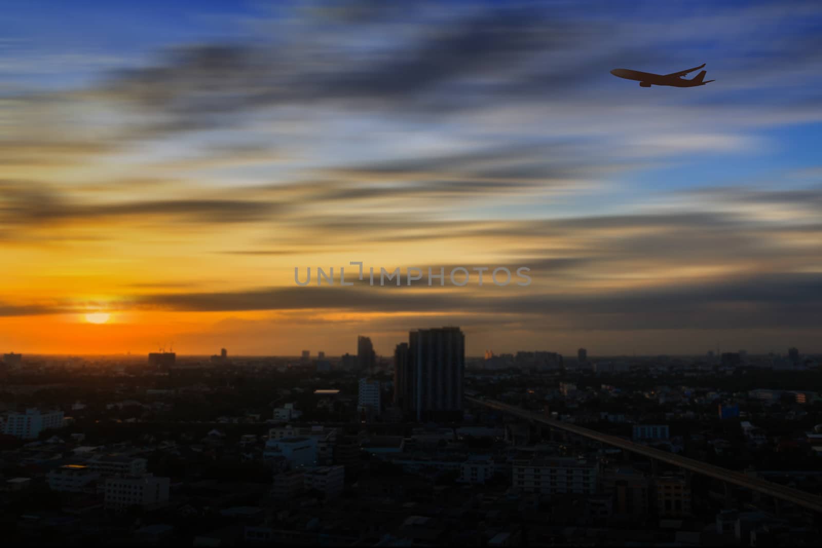 Silhouette of airplane flying in a sunset sky over the city at sunrise