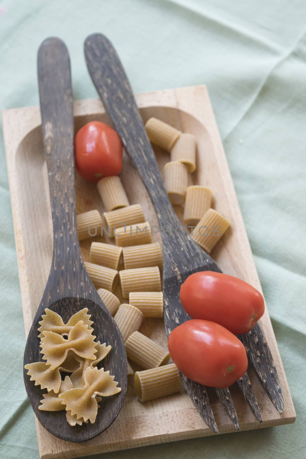 wholemeal butterfly pasta on a wooden ladle and fresh cherry tomatoes