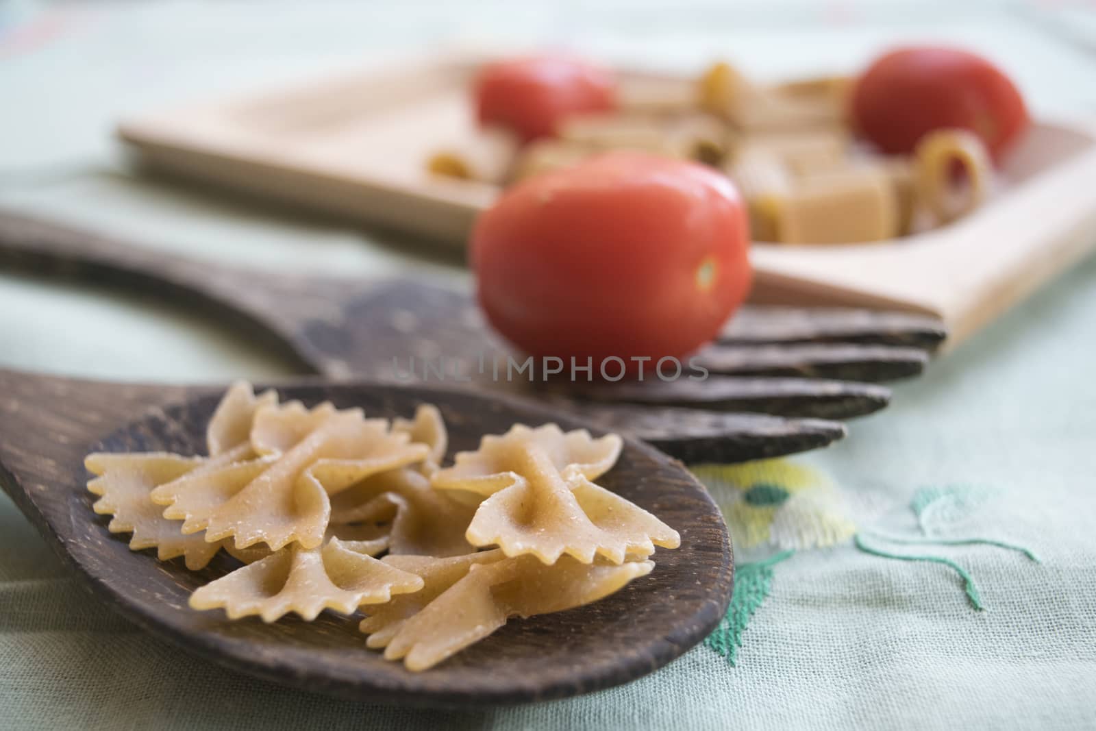 wholemeal butterfly pasta on a wooden ladle and fresh cherry tomatoes