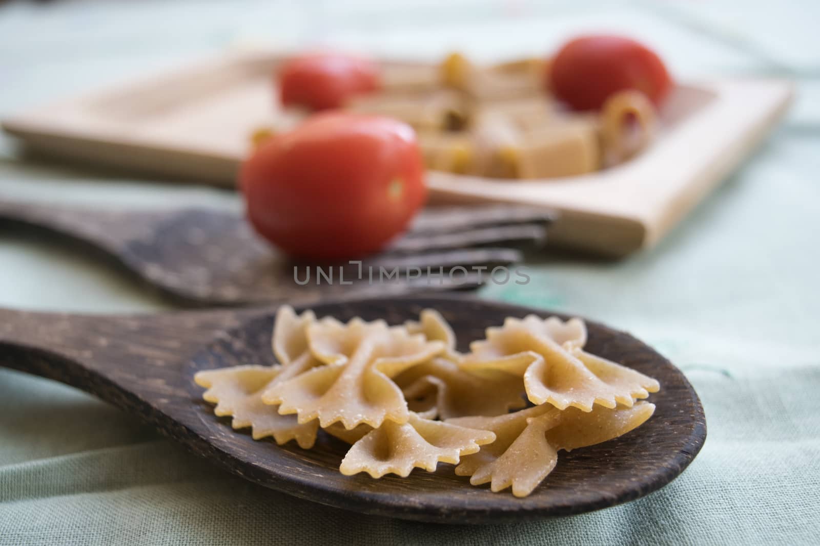 wholemeal butterfly pasta on a wooden ladle and fresh cherry tomatoes