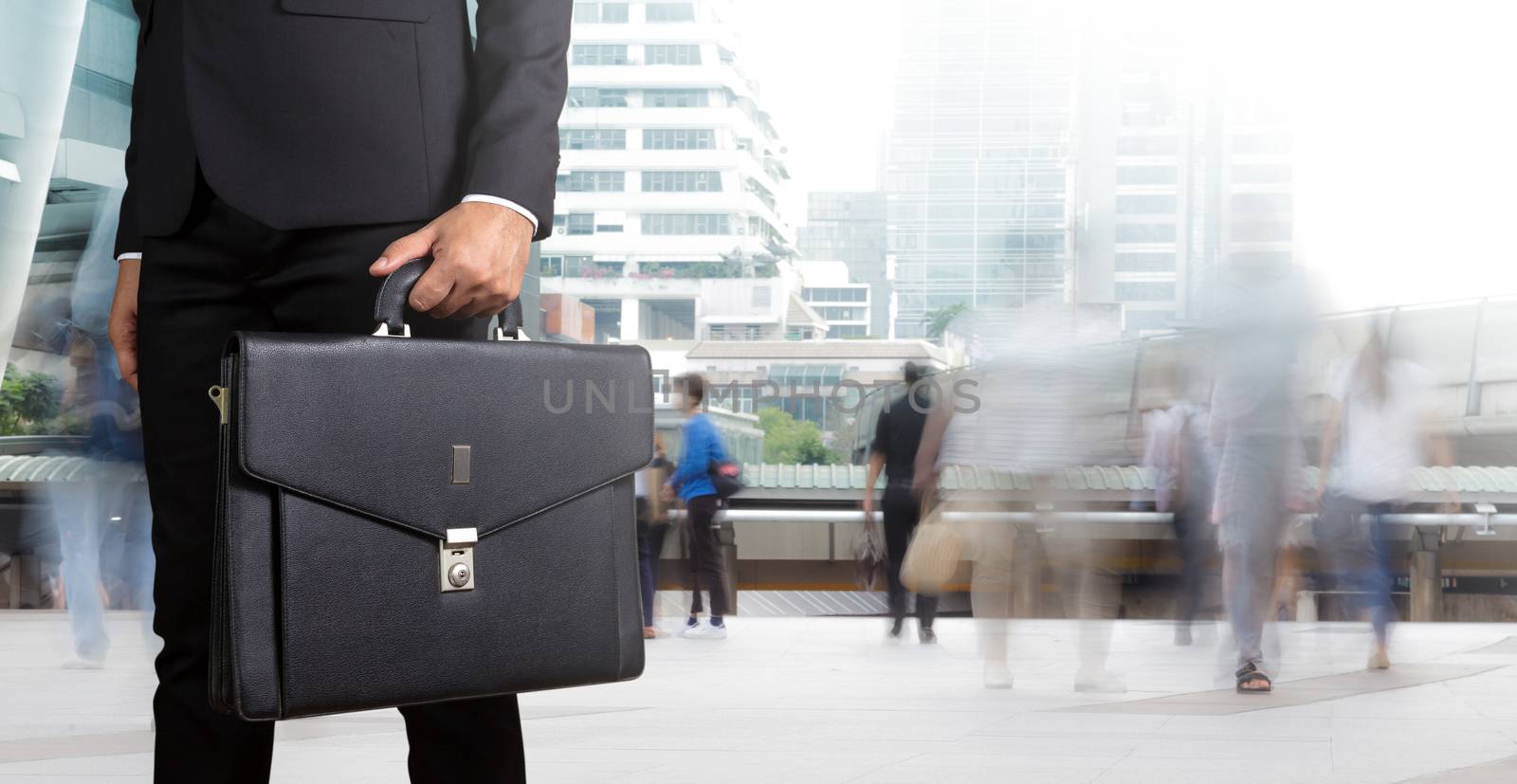 Businessman holding a briefcase with people walking in motion blur in the city background