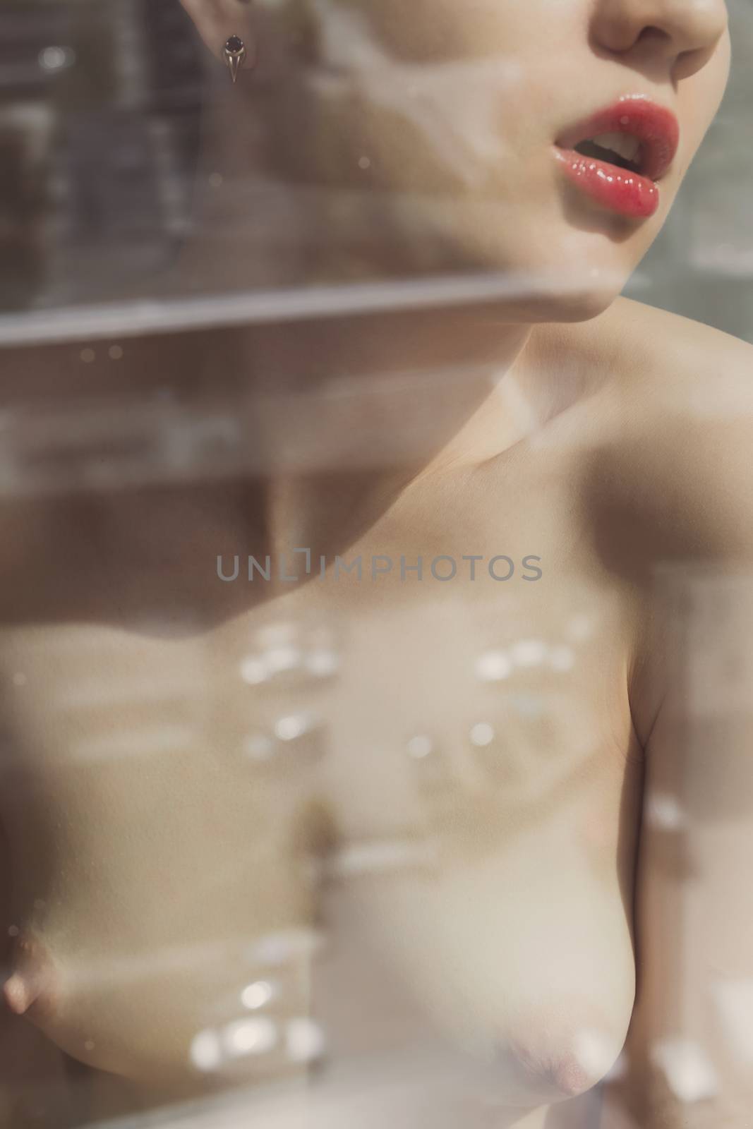 Crop view through glass of anonymous young woman with naked chest