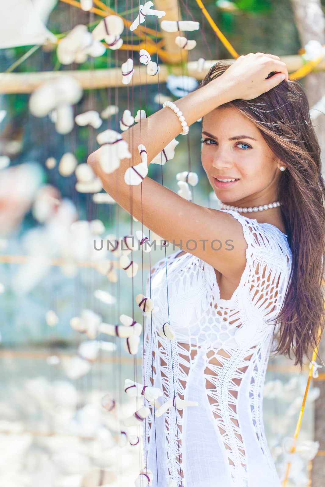 Beautiful woman in white dress on vacation touching a garland of shells and corals