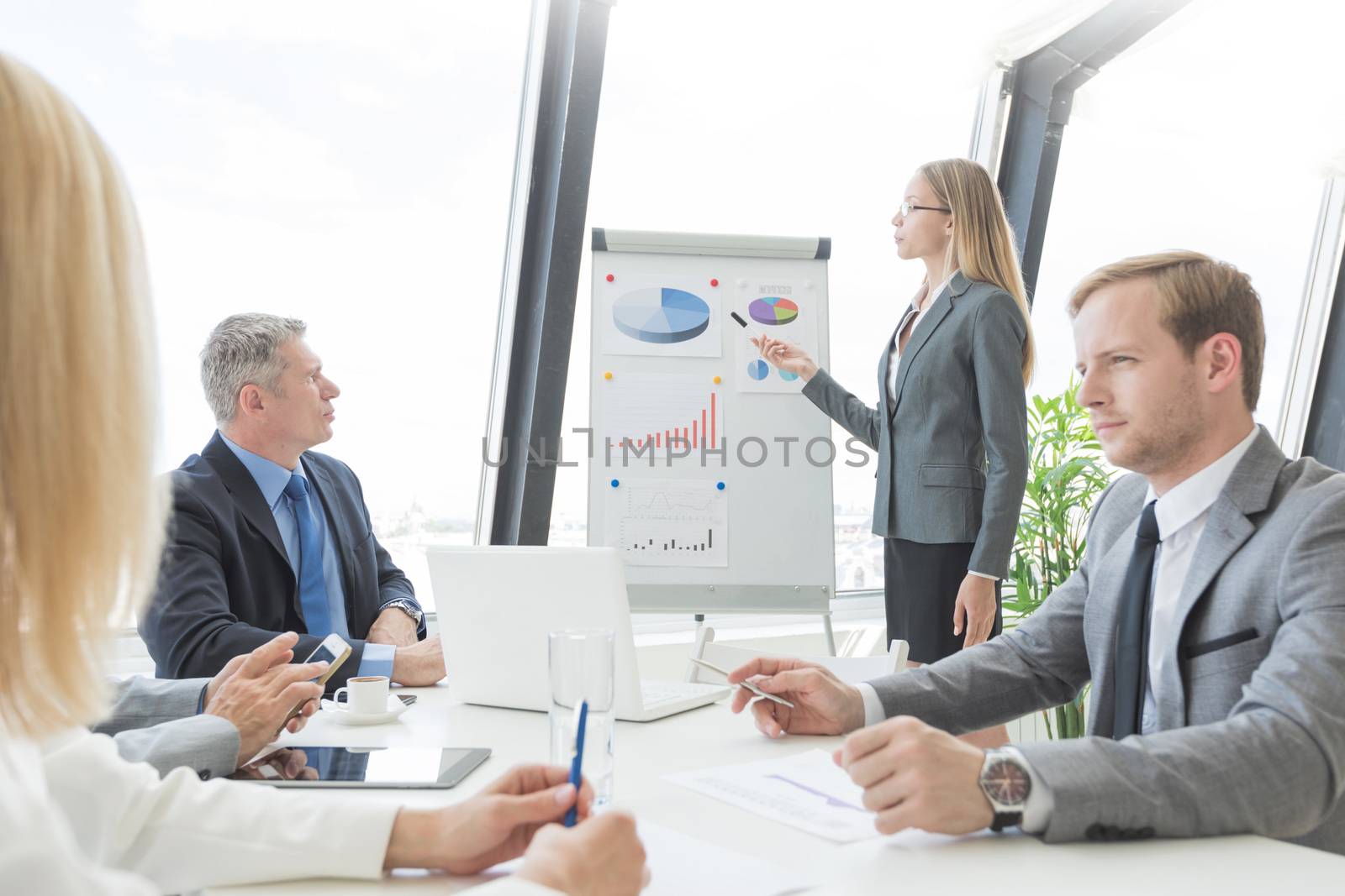 Business presentation of statistics, business woman pointing at flipchart, team of people at meeting table watching