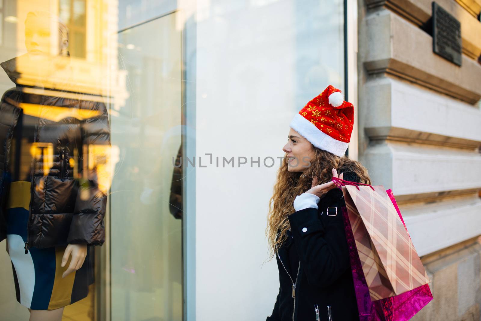 Young attractive woman with santa claus hat in front of shopping window looking to buy something
