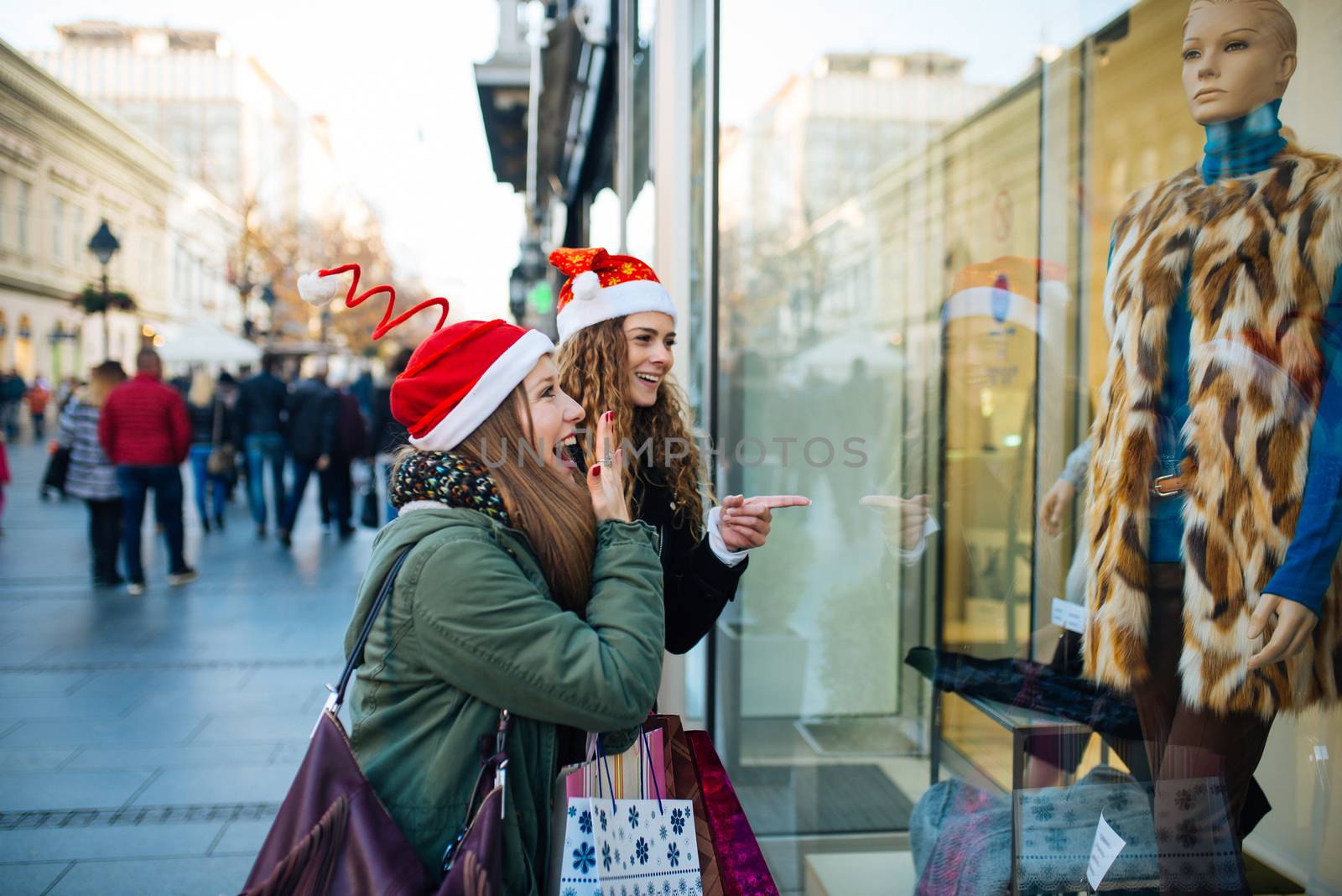 Young attractive woman with santa claus hat in front of shopping window looking to buy something.