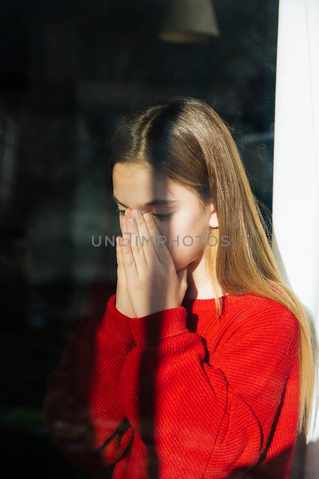 A sad and depressed cute little girl alone near the window. Outdoor portrait of a sad teenage girl.