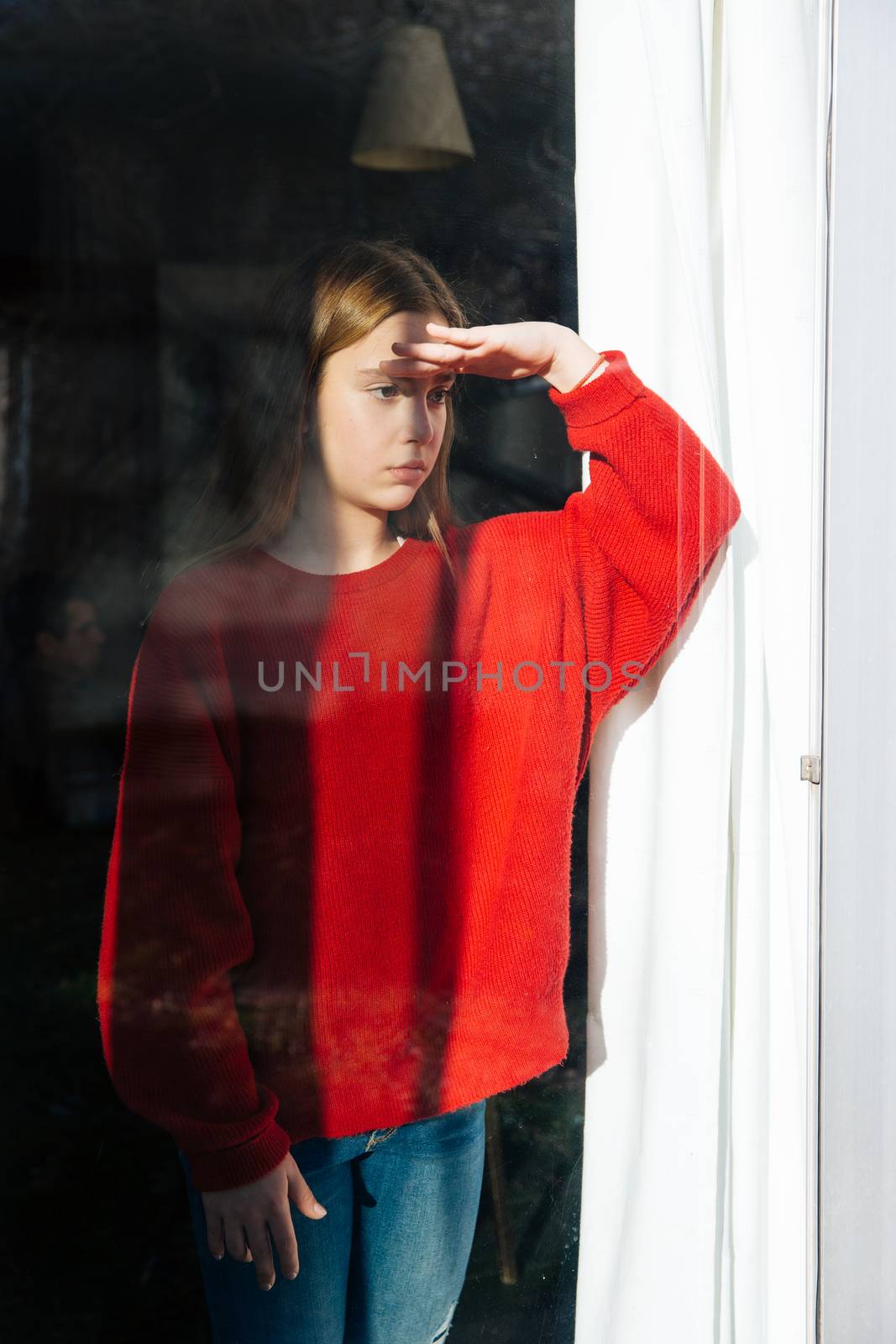 A sad and depressed cute little girl alone near the window. Outdoor portrait of a sad teenage girl.