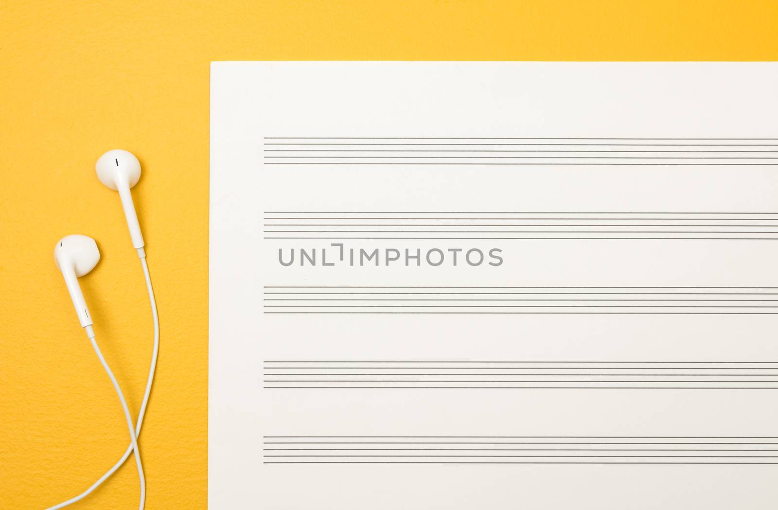 White earphones and blank music paper sheet on vibrant yellow background.