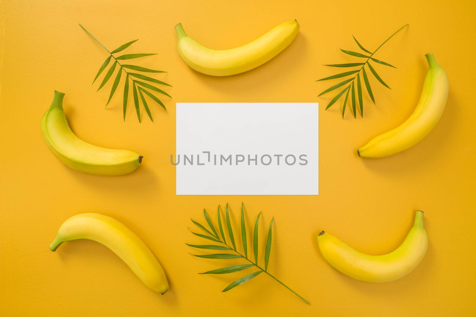 Bananas, palm leaves and blank paper sheet on bright yellow background. Tropical summer theme.