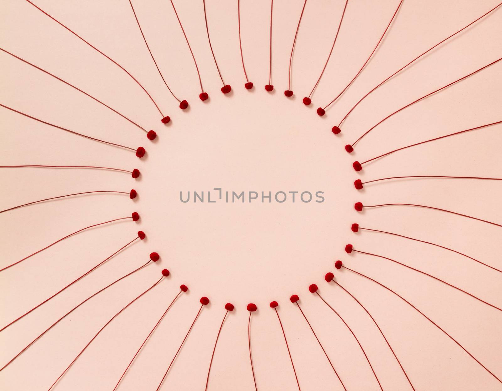 Round frame made of delicate red flowers, on pastel pink background.