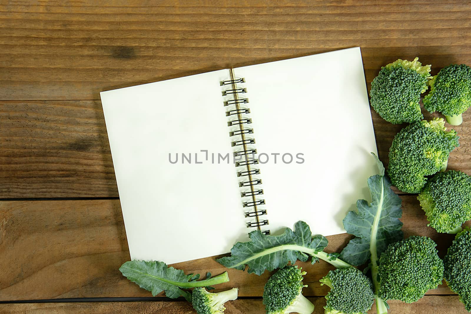 blank notebook with fresh broccoli on wooden table by rakoptonLPN