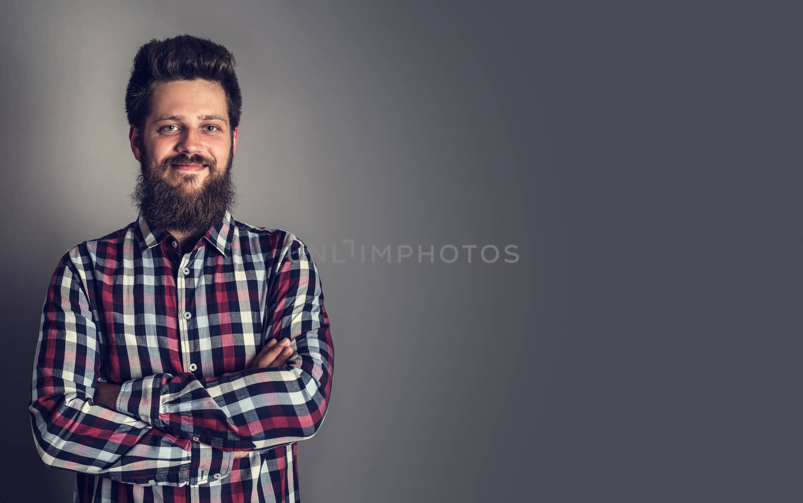 Smiling bearded man in checked shirt, portrait, studio shot on gray background