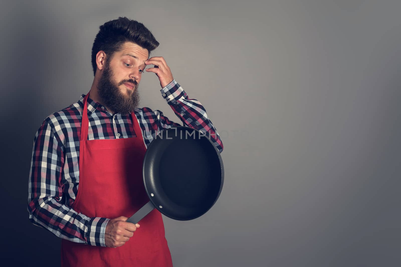 Man in red apron looking at frying pan and thinking