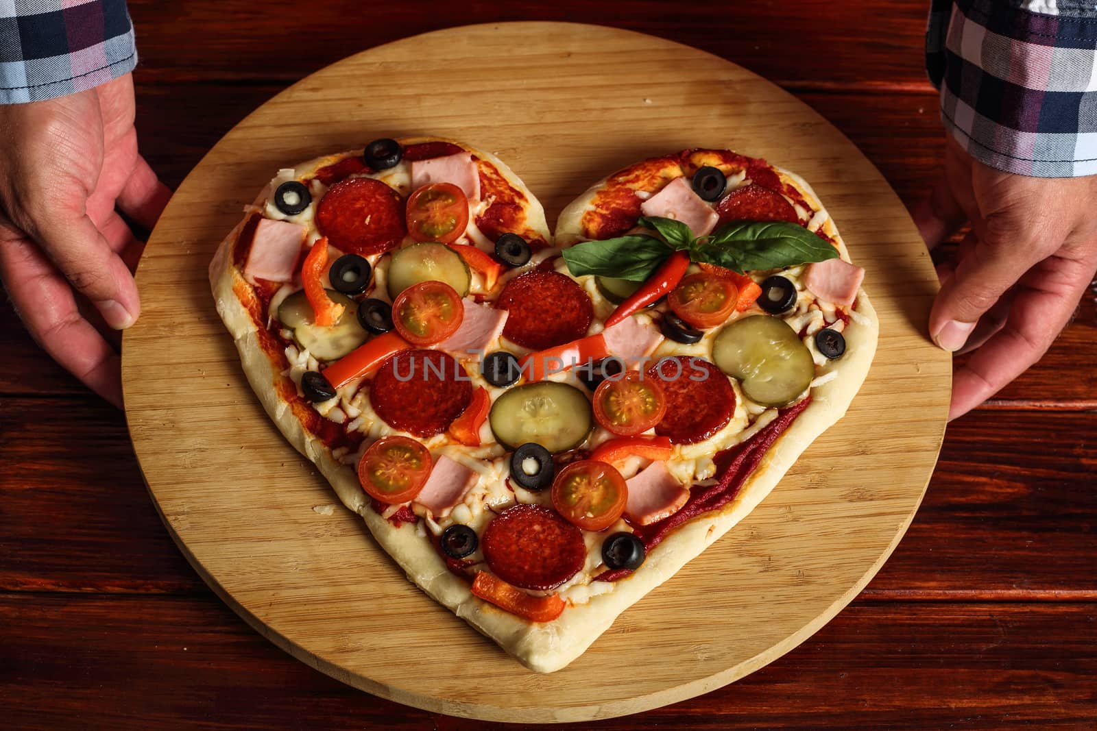 Male hands holding heart shapes pizza
