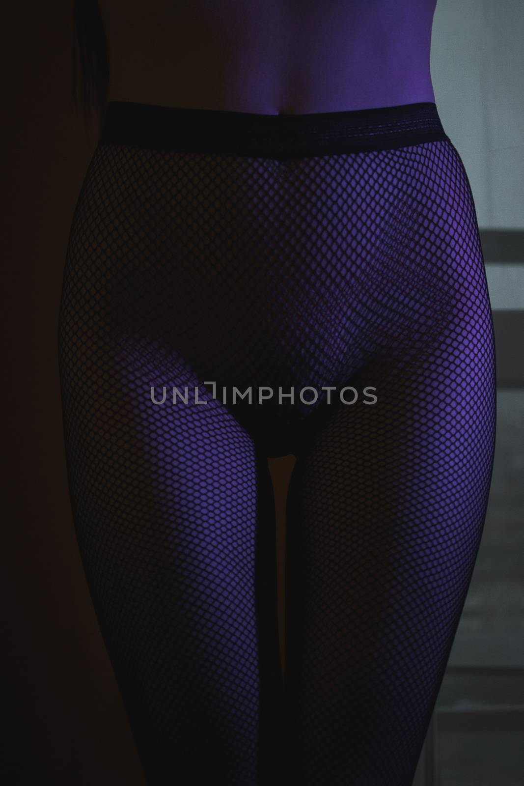 Crop shot of curvy female hips in fishnet tights standing in dark neon lights