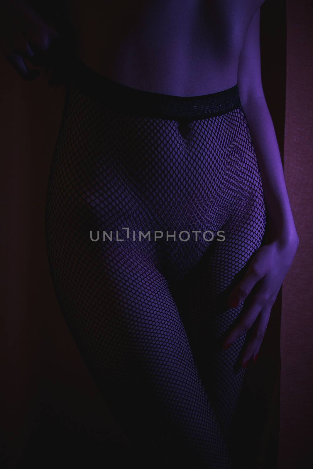 Crop shot of curvy female hips in fishnet tights standing in dark neon lights