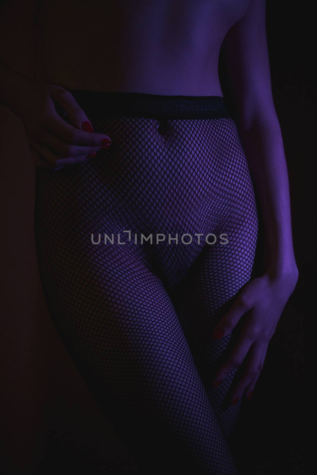Crop shot of curvy female hips in fishnet tights standing in dark neon lights