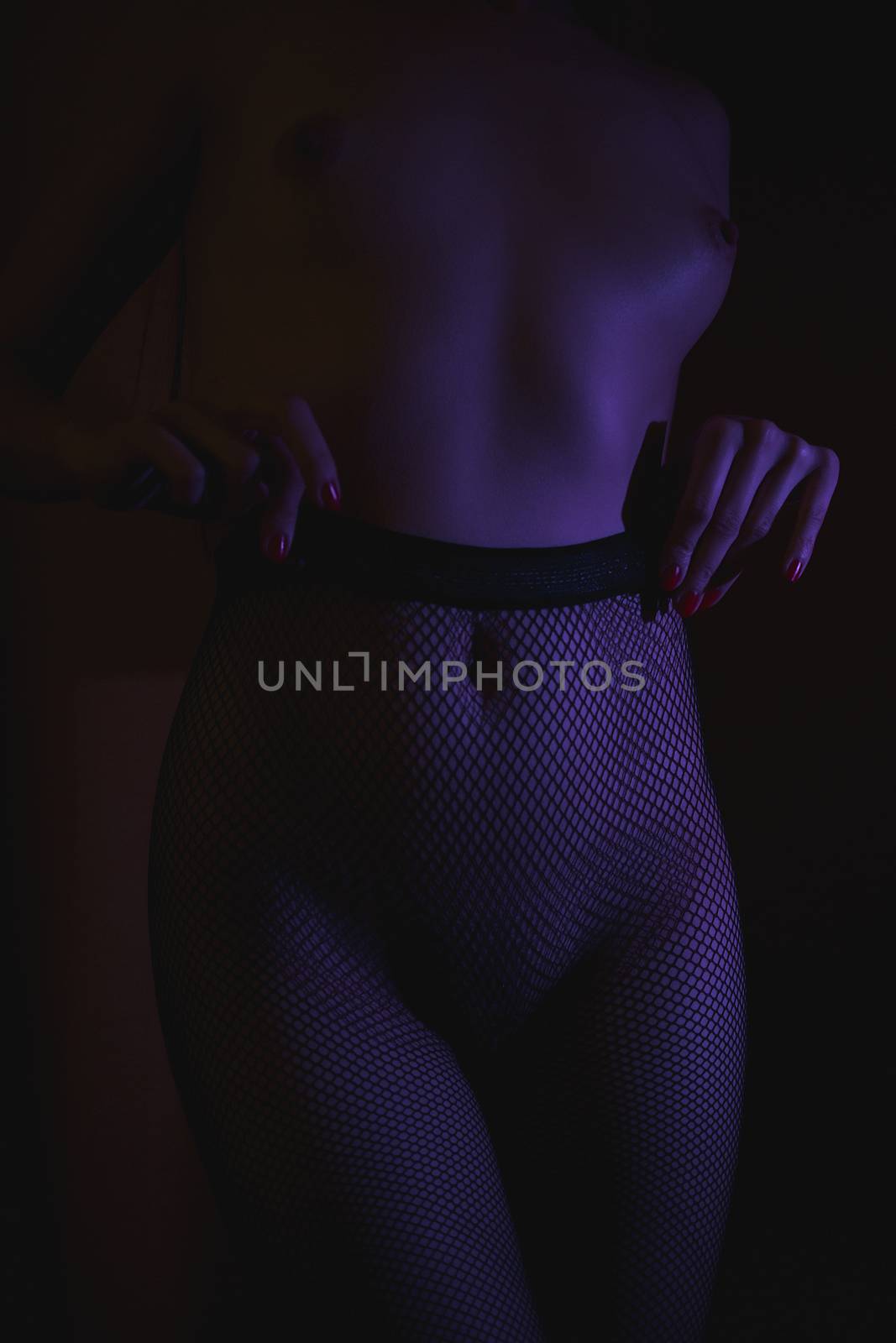 Crop shot of curvy female hips in fishnet tights standing in dark neon lights