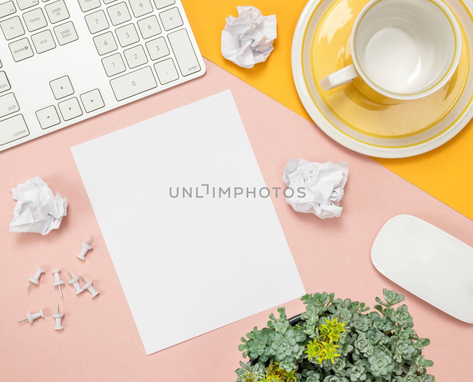 Bright summer home office workspace with blank sheet of paper in the middle. Flat lay composition on pink and yellow background.