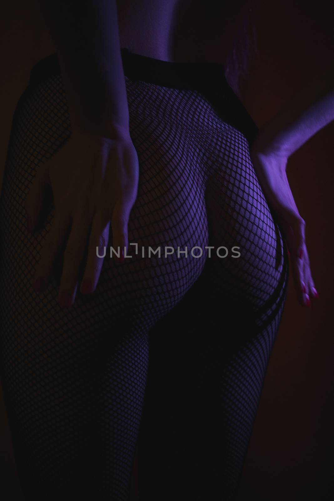 Back view of crop female with sexual ass in stockings in grid standing in darkness