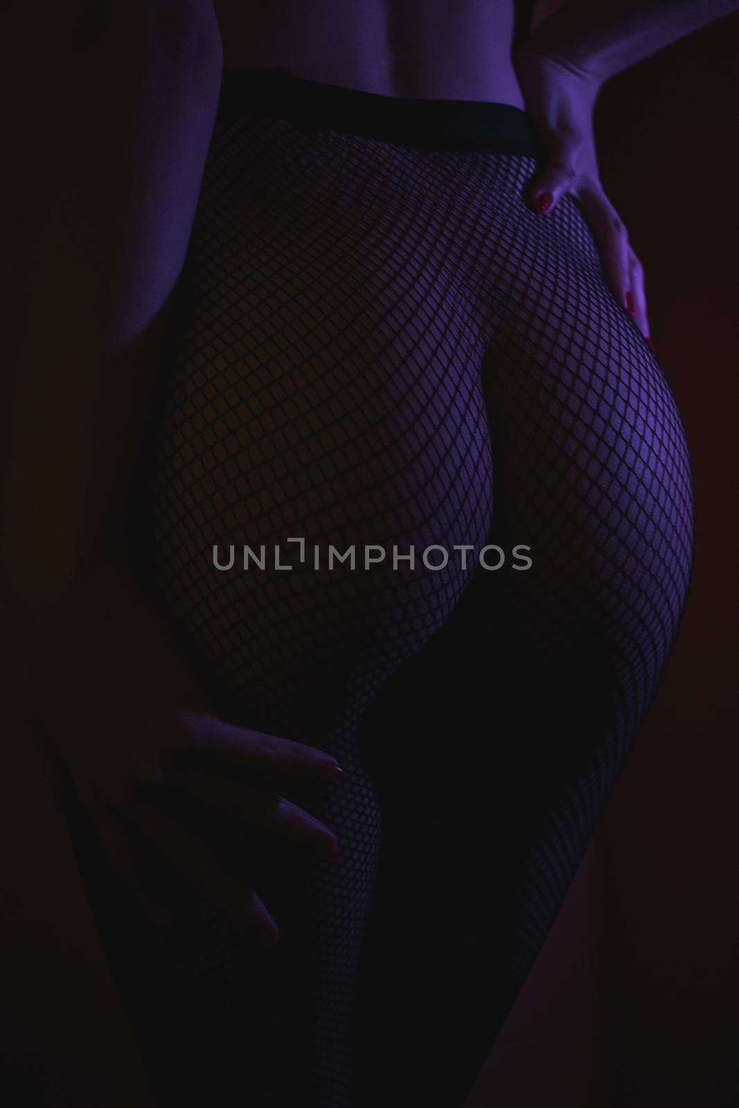 Back view of crop female with sexual ass in stockings in grid standing in darkness
