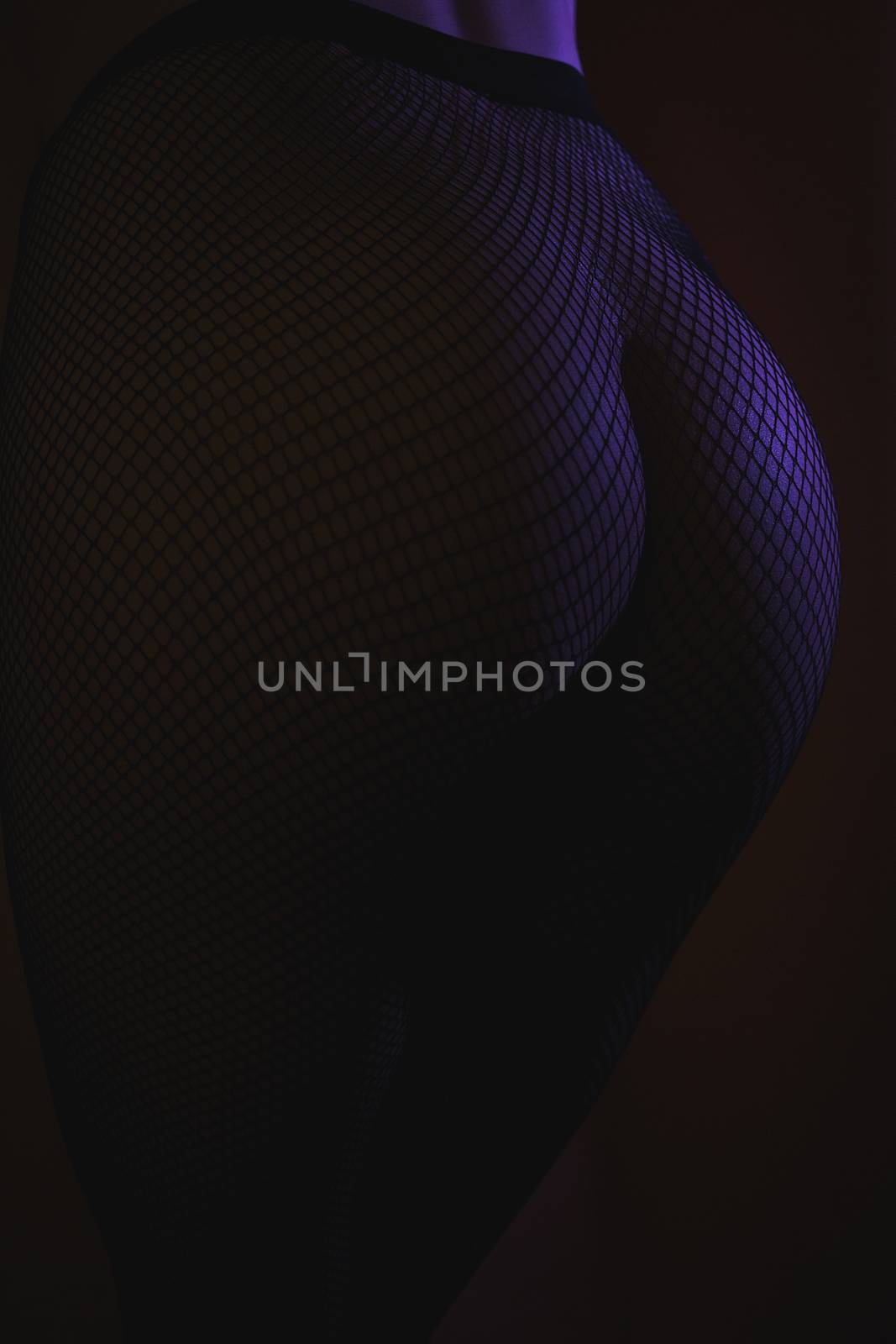 Back view of crop female with sexual ass in stockings in grid standing in darkness